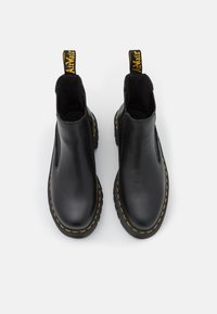 Zwarte leren enkelboots met elastische zijkanten, gele stiksels en een merklabel aan de achterkant. Glad materiaal, ronde neus.