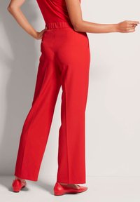 Rote, weit geschnittene Hose mit elastischem Bund und seitlichen Taschen. Der Stoff wirkt glatt und leicht und wird mit passenden Ballerinas kombiniert.