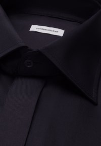 Chemise noire à col pointu et patte de boutonnage, avec une étiquette de marque blanche Seidensticker à l'intérieur du col.