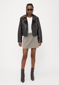 Brun læder cropped jakke med faux pelskrave, hvid skjorte, ternet mini skirt og knæhøje brune hæle støvler. Solbriller inkluderet.
