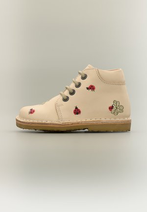 Bottine beige en cuir pour enfants avec fermeture à lacets, décorée de coccinelles rouges brodées et de feuilles de trèfle vertes, semelle plate.