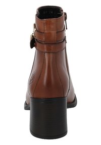 Bota de tobillo de cuero marrón con tacón apilado, cremallera lateral y hebillas decorativas. Textura lisa con un acabado ligeramente brillante.