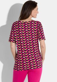 Korte mouwen top met een geometrisch patroon in roze, zwart en nude kleuren op een lichtgewicht materiaal, gecombineerd met roze leggings.