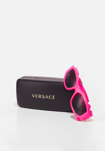 Rosa plastsolbriller med svarte linser, med et geometrisk design, sammen med et svart etui med en gull "VERSACE" logo.