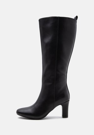 Botte en cuir noire montant jusqu'au genou avec bout pointu, talon bloc et languette à l'arrière, affichée en profil sur fond blanc.