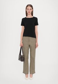 Schwarzes Kurzarmoberteil, karierte beigen Hosen und weiße High Heels. Hält eine dunkelbraune Handtasche. Einfaches und strukturiertes Design mit klaren Linien.