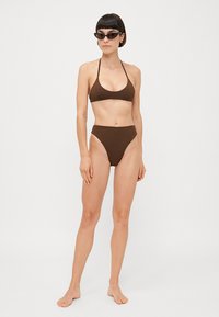 Hnedý bikiny set pozostávajúci z trojuholníkového topu a nohavičiek s vysokým pásom, vyrobený z hladkého materiálu. Navrhnutý s minimálnymi popruhmi a bezšvovými okrajmi.