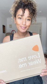 Caixa de cartão com uma superfície lisa e bege; apresenta texto impresso em branco e laranja. A caixa exibe a marca "Zalando" de forma proeminente.