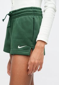 Πράσινα σορτς Nike με ρυθμιζόμενο κορδόνι στη μέση, πλαϊνές τσέπες και λευκό λογότυπο. Το ύφασμα είναι απαλό με λείο υφή και πλαϊνές σχισμές.