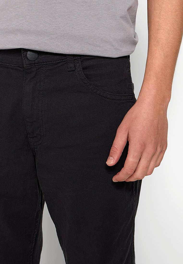 Schwarze Jeans mit schmalem Schnitt, ausgestattet mit einem Knopf- und Reißverschluss, Fronttaschen und sichtbaren Nähten. Material: Baumwollmischung.