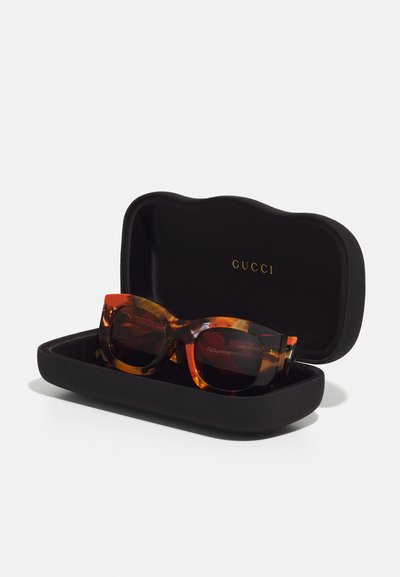 Gucci prillid, millel on kilpkonnakuju muster mustas ümmarguses karbis. Omavad tumedaid läätsi ja graveeritud brändi detaile varrel.