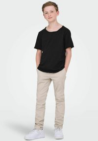 Czarna koszulka z krótkim rękawem i okrągłym dekoltem, zestawiona z beżowymi spodniami i białymi trampkami. Prosty design i luźny krój.