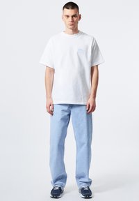 Camiseta de algodón blanca con un corte relajado, que presenta un estampado en azul claro. Combinada con jeans rectos de color azul claro y zapatillas navy.