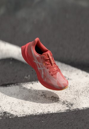 Leichter Laufschuh in leuchtendem Koralle mit einem strukturierten Mesh-Obermaterial, reflektierenden Akzenten und einer gepolsterten Sohle, die über einer Laufbahn schwebt.