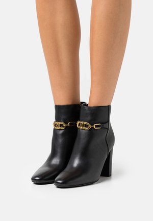 Black leather ankle boots with a pointed toe, gold chain accent, and a high block heel. Smooth texture and sleek design.