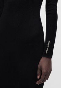 Gros plan d'une personne portant une robe noire à manches longues avec le texte « armani exchange » en blanc sur la manche près du poignet.