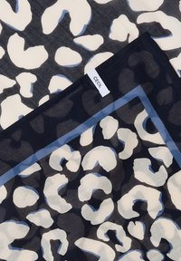 Tkanina z nieregularnym białym i niebieskim wzorem w panterkę na czarnym tle, z naszytą białą metką z napisem "CECIL".