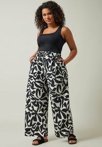 Débardeur noir associé à un pantalon large à motifs amples, blanc avec des formes abstraites noires. Le mannequin porte des sandales noires.