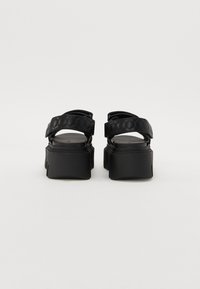 Black platform sandals featuring thick soles, adjustable straps with a textured pattern, and a minimalist design.