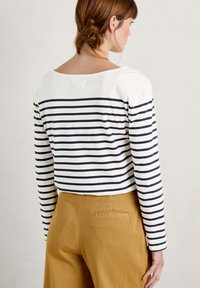 Top de manga larga con rayas horizontales en azul marino y blanco, con un escote amplio. Combinado con pantalones color mostaza. Tejido suave.