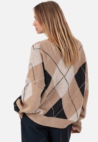 Pull épais en beige, noir et crème avec un motif en losange. Texture douce et coupe ample, avec des poignets et un ourlet côtelés.