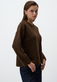 Maglione marrone, con trama, a maniche lunghe e scollatura rotonda, abbinato a jeans blu scuro. Design semplice, con vestibilità leggermente cropped.