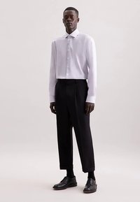 Wit overhemd met knopen en een lichte glans, gecombineerd met zwarte, op maat gemaakte broek en zwarte leren schoenen. Strakke lijnen met een moderne pasvorm.