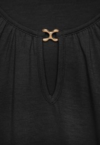Black top featuring a small keyhole opening with a decorative gold accent. Soft fabric with a gathered texture around the neckline.