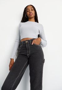 Gaiši pelēks, īss garām piedurknēm tops, apvienots ar augsta vidukļa melno džinsu biksēm, kas izceļ redzamas šuvju detaļas un sānu kabatas.