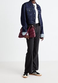 Denim cropped jacket with blue fabric, two front pockets, paired with gray pinstriped trousers and black sneakers with cream accents. Burgundy handbag.