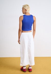 Blå randig crop top, vita vida byxor och röda skor med synlig märkning. Hudtextur och kort ljust hår. Enkel design.
