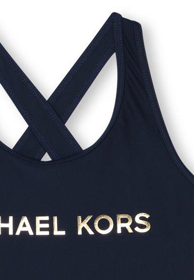 Costume da bagno blu navy con logo dorato "MICHAEL KORS". Ha un design elegante con spalline incrociate e tessuto liscio e testurizzato.