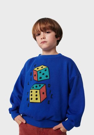 Blaues Sweatshirt mit einem Grafikdesign von zwei Würfeln in Gelb, Rot und Türkis, mit dem Text "WÜRFELN" in Schwarz. Baumwollmaterial, lockere Passform.