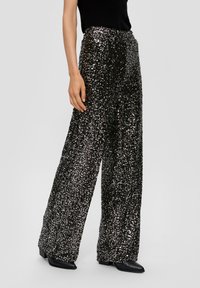 Hochgeschnittene, weit geschnittene Hose, die mit schwarzen Pailletten bedeckt ist, mit einer glatten Textur und subtilen Glanz. Kombiniert mit eleganten schwarzen Schuhen.