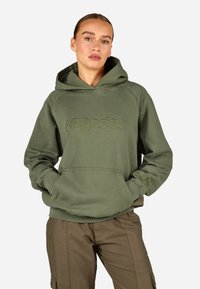 Πράσινο φούτερ με καγκουρό τσέπη και ραμμένα μανίκια. Διαθέτει ανάγλυφο λογότυπο μπροστά. Λείο βαμβακερό ύφασμα. Συνδυάζεται με καφέ παντελόνι.