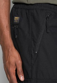 Zwarte shorts van gestructureerde stof met ritszakken en een elastische tailleband. Een label is zichtbaar aan de rechterkant.