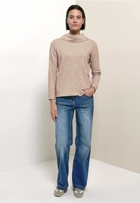 Haut beige à manches longues avec un col bénitier, associé à un jean flare bleu clair et des baskets grises. Design simple et texture douce.