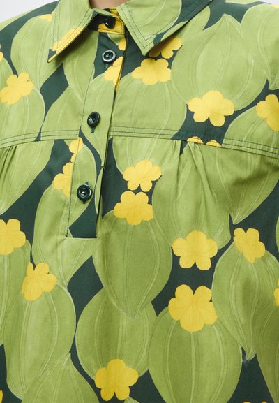 Chemise avec un motif feuillu vert et des fleurs jaunes, boutons vert foncé sur le devant et col pointu.