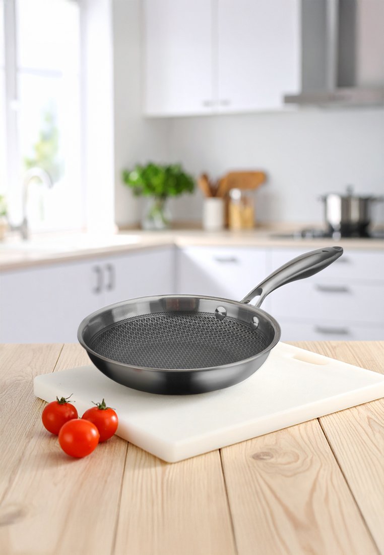 Pánev s nepřilnavým povrchem, s texturovaným černým interiérem, stříbrným okrajem a ergonomickou rukojetí, umístěná na prkénku vedle cherry rajčat.