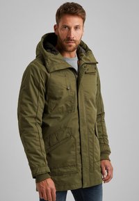 Maslinasto zelena izolirana zimska jakna s kapuljačom, koja ima zatvaranje na patentni zatvarač, više prednjih džepova i rebraste manšete za dodatnu toplinu.