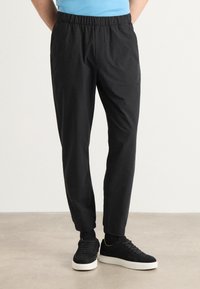 Zwarte casual broek met elastische tailleband, tapered fit en zijzakken, gecombineerd met zwarte sneakers met witte zolen en een minimalistisch ontwerp.