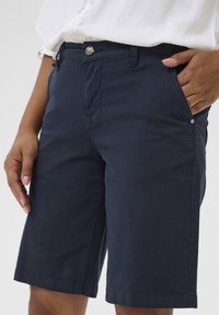 Mörkblå knälånga shorts i bomull med knappstängning och sidofickor. Har en mjuk textur och en enkel design.