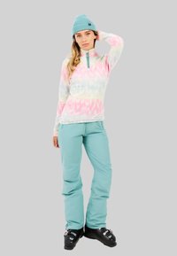 Lichtgewicht, pastelgekleurde tie-dye pullover met hoge kraag, turquoise skibroek en zwarte skibotten, met een relaxte pasvorm en een gestructureerde stof.