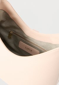 Γυναικεία τσάντα χειρός από δέρμα σε ανοιχτό ροζ χρώμα με λεία υφή, που διαθέτει μπεζ φόδρα, εσωτερική τσέπη με φερμουάρ και δερμάτινη ετικέτα με το λογότυπο της μάρκας.