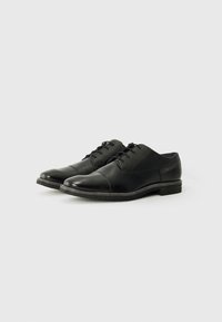 Zapatos de vestir de cuero negro con un acabado suave, sistema de cordones y costuras sutiles. Presentan un tacón bajo apilado y suela texturizada.