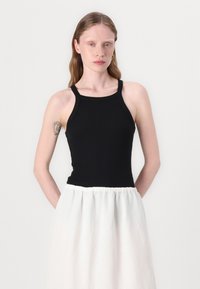 Schwarzes, tailliertes Tanktop mit breiten Trägern, kombiniert mit einem weißen Rock mit gerafftem Bund. Glatte, gerippte Textur, minimalistisches Design.