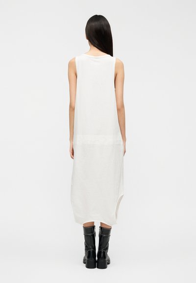 Rochie albă fără mâneci, realizată dintr-un material moale, cu decolteu rotund și tiv asimetric. Purtați-o cu cizme negre până la genunchi.