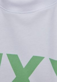 Camiseta de algodón blanca con letras grandes impresas en verde. Textura suave, diseño de cuello redondo sin embellishments ni patrones visibles.