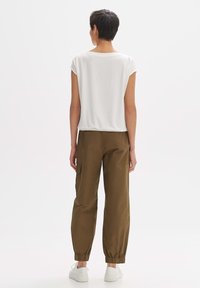 Top bianco a maniche corte abbinato a pantaloni cargo verdi oliva con polsini elastici e tasche, completato da sneakers bianche.