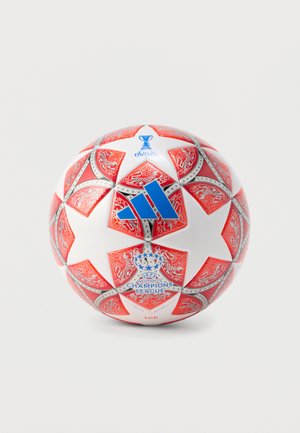 Biała piłka nożna z czerwonymi i srebrnymi ozdobnymi panelami w kształcie gwiazdy, z logo Ligi Mistrzyń UEFA kobiet oraz niebieskim logo Adidas.